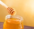 Honey jar on wood table and golden background with wooden dipper on top with drop honey