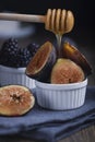Honey pouring of fresh cuted organic figs and blackberry on white cupcake baking dishes on rustic wooden background with dark blue