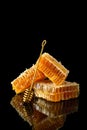 Honeycomb with natural honey and golden dipper on black background with reflection. Side view, close up. Natural, organic food.
