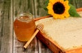 Honeycomb in a wooden frame decorated with sunflower and glass jar of honey on a wooden background