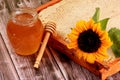 Honeycomb in a wooden frame decorated with sunflower and glass jar of honey on a wooden background