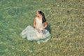 Honeymoon travel concept. Fashion and beauty. Girl sitting in sea water. Bride on sunny summer day on seascape Royalty Free Stock Photo