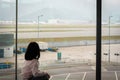 HONG KONG, CHINA - JANUARY 14, 2019: The back view of girl kid sitting and watching airport runway at the airport glass window in