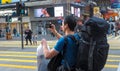 HONGKONG, CHINA - December 9 2016: Young man with luggage bag on city street with map in Hong Kong, taking photo with smart phone Royalty Free Stock Photo