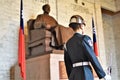 An honor guard in full ceremonial uniform stands beside a bronze statue