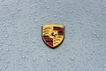 Hood emblem of sports car Porsche in raindrops on the grey background.