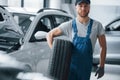 Hood is opened on the other car. Mechanic holding a tire at the repair garage. Replacement of winter and summer tires Royalty Free Stock Photo