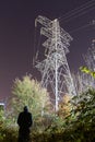 A hooded figure, back to camera. Looking up at a electricty pylon on a winters night Royalty Free Stock Photo