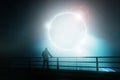 A hooded figure, standing with back to camera on a bridge, looking at a glowing, mystic, science fiction portal. On a foggy night Royalty Free Stock Photo