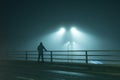 A hooded figure, standing with back to camera on a bridge, looking out at street lights. On a foggy night Royalty Free Stock Photo