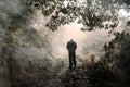 A hooded figure walking away from the camera on a misty woodland path with shoulders hunched and looking down Royalty Free Stock Photo