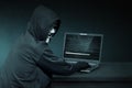 Hooded hacker with anonymous mask using laptop to steal data Royalty Free Stock Photo