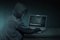 Hooded hacker with anonymous mask using laptop to steal data Royalty Free Stock Photo