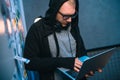 hooded hacker developing malware with laptop