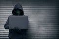 Hooded hacker with mask holding laptop while typing