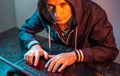 Hooded hacker is typing on a laptop keyboard in a dark room under a neon light. Cybercrime fraud and identity theft Royalty Free Stock Photo