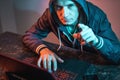 Hooded hacker is typing on a laptop keyboard in a dark room under a neon light. Cybercrime fraud and identity theft Royalty Free Stock Photo