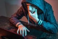 Hooded hacker is typing on a laptop keyboard in a dark room under a neon light. Cybercrime fraud and identity theft Royalty Free Stock Photo