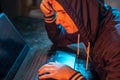 Hooded hacker is typing on a laptop keyboard in a dark room under a neon light. Cybercrime fraud and identity theft Royalty Free Stock Photo