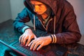 Hooded hacker is typing on a laptop keyboard in a dark room under a neon light. Cybercrime fraud and identity theft Royalty Free Stock Photo