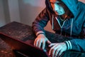 Hooded hacker is typing on a laptop keyboard in a dark room under a neon light. Cybercrime fraud and identity theft Royalty Free Stock Photo