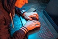 Hooded hacker is typing on a laptop keyboard in a dark room under a neon light. Cybercrime fraud and identity theft Royalty Free Stock Photo
