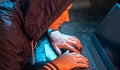 Hooded hacker is typing on a laptop keyboard in a dark room under a neon light. Cybercrime fraud and identity theft Royalty Free Stock Photo