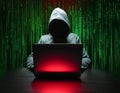 A hooded hacker working on a laptop with a red screen, surrounded by green binary code