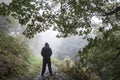A hooded man standing with his back to the camera on a woodland path on a moody foggy autumn day. Royalty Free Stock Photo