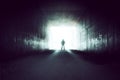 A hooded silhouetted figure standing on the edge of a tunnel looking out onto a bright overexposed light Royalty Free Stock Photo