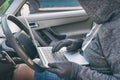 Hooded thief tries to break the car`s security systems with laptop Royalty Free Stock Photo