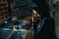 Hoodie hacker looking at stolen bank cards.