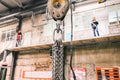 Hook on a metal chain in industrial production. Equipment for transporting heavy loads in the factory. Workers are