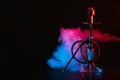 Hookah with a glass flask and a metal bowl shisha with colored smoke on the table Royalty Free Stock Photo