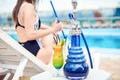 Hookah or shisha or kalian and a tropical summer refreshing alcoholic coctail in front of swimming pool and a beautiful