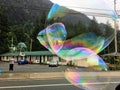A man blowing huge bubbles along the side of the road, trying to sell bubble makers to people passing by
