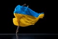 Hope. Young graceful classic ballerina dancing with cloth painted in blue and yellow colors of Ukraine flag on dark