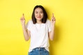 Hopeful asian girl smiling optimistic, feeling lucky, cross fingers and making wish, looking up dreamy, standing over