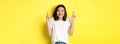 Hopeful asian girl smiling optimistic, feeling lucky, cross fingers and making wish, standing over yellow background