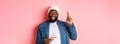 Hopeful Black guy celebrating birthday, making wish with fingers crossed, holding bday cake with candle, standing