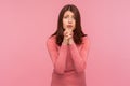 Hopeful brunette woman in pink sweater holding hands in prayer, asking for forgiveness looking at camera with regard, need help Royalty Free Stock Photo