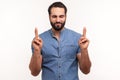 Hopeful dreamy man with beard in blue shirt crossing fingers and closing eyes making wish, believing in miracle, hope in success Royalty Free Stock Photo