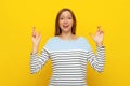 Hopeful fair-haired girl wishing, holds fingers crossed and praying, pleading to achieve smth, standing over yellow background Royalty Free Stock Photo