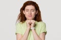 Hopeful redhead woman clenching fists making wish isolated on background Royalty Free Stock Photo