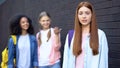 Hopeless bullying victim looking camera, female classmates discussing behind