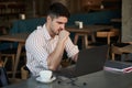 Hopes that his business plan will reach success. Adult man sits in cafe at daytime and using the laptop for the remote