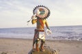 Hopi Kachina doll holding objects on beach with ocean in the background