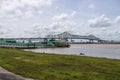 The Horace Wilkinson Bridge over the flowing waters off the Mississippi River with boats on the water, lush green grass and clouds