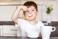 Horiontal portrait of attractive male child eats delicious porridge with milk, dressed in casual white t shirt, has good appetite