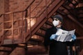 Horiontal shot of pensive man poses with newspaper, wears protective mask and rubber gloves, looks aside, thinks about self